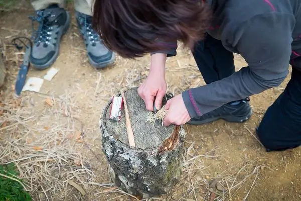 Person bereitet Zunder auf einem Baumstumpf vor beim Survival Training