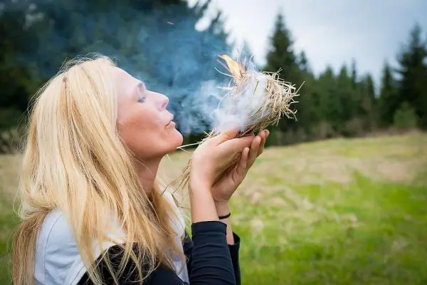 Person bläst in ein Nest aus Gras und Zunder