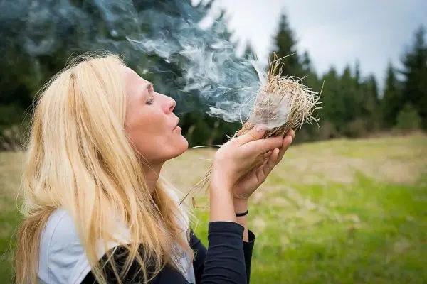 Person bläst Rauch aus einer Handvoll trockenem Gras