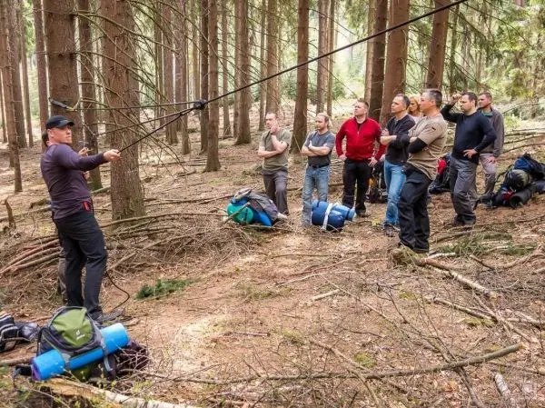 Person demonstriert eine Technik im Wald, Gruppe schaut zu beim Überlebenstraining