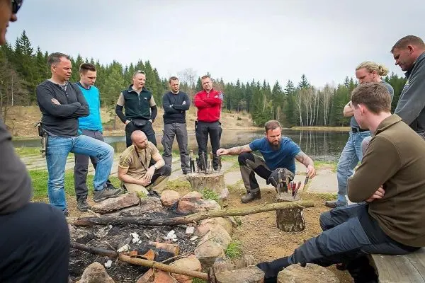 Person erklärt Techniken am Lagerfeuer, Gruppe hört aufmerksam zu beim Überlebenstraining