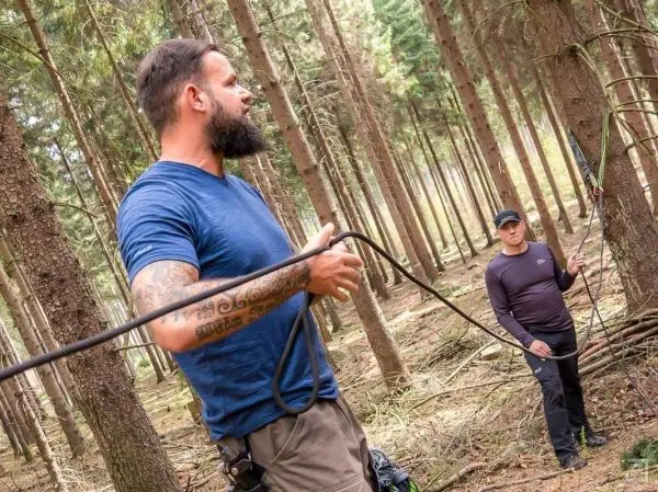 Person hält ein Seil und spricht mit einer anderen Person im Wald
