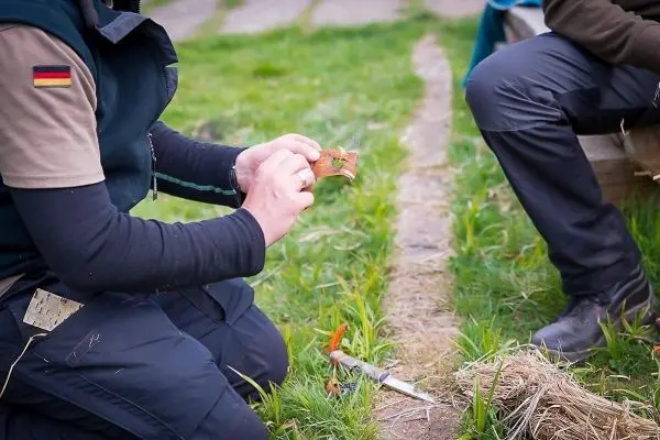 Person hält ein Stück Holz in der Hand und zeigt es einem anderen