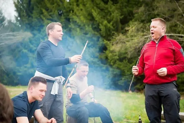 Person hält Stock über Feuer, andere Personen sitzen daneben
