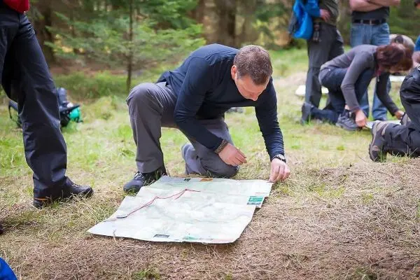 Person kniet und studiert eine Karte im Wald beim Überlebenstraining