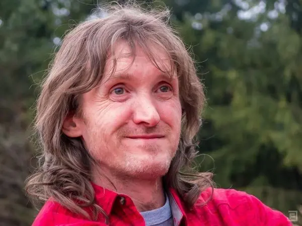 Person mit langen Haaren und rotem Hemd schaut lächelnd in die Kamera