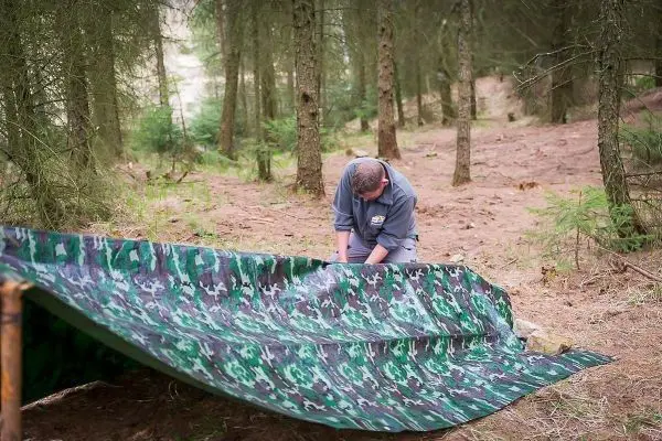Person richtet eine Tarnplane im Wald aus