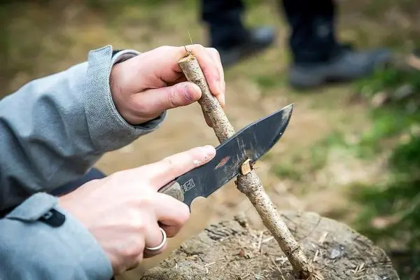 Person schnitzt mit einem Messer einen Stock auf einem Holzblock