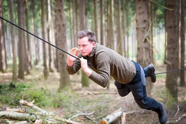 Person schwingt an einer selbstgebauten Seilbrücke durch den Wald