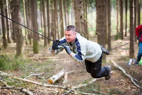 Person schwingt an einer selbstgebauten Seilbrücke im Wald