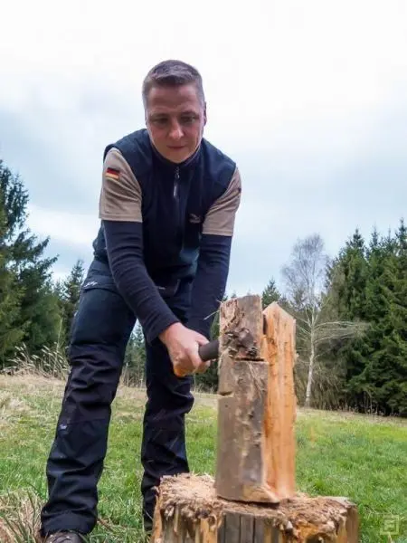 Person spaltet Holz mit einer Axt im Freien