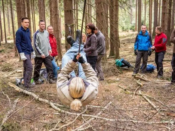 Person überquert an einer selbstgebauten Seilbrücke im Wald, Gruppe beobachtet