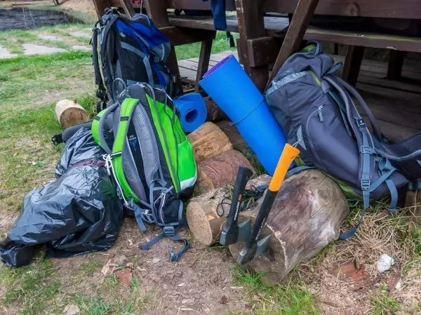 Rucksäcke und Werkzeuge liegen neben Holzstämmen auf dem Boden