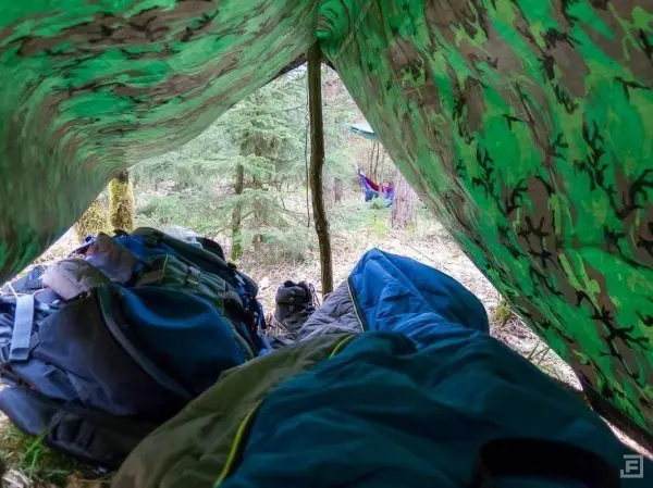 Tarp-Notunterkunft mit Rucksäcken und Schlafsäcken im Inneren