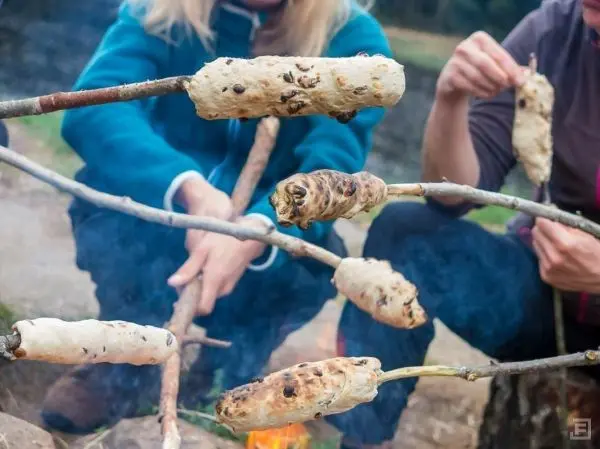 Teigstücke rösten über einem kleinen Feuer auf Stockspießen