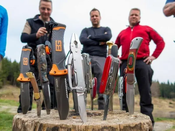 Verschiedene Messer stehen auf einem Baumstumpf, während Personen im Hintergrund stehen