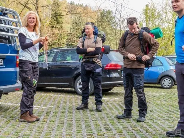 Vier Personen mit Rucksäcken stehen auf einem Parkplatz neben Autos