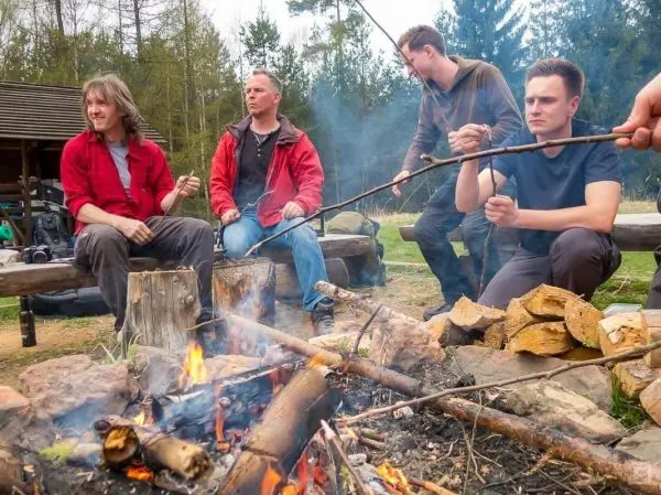 Vier Personen sitzen um ein Lagerfeuer und halten Stockspieße über die Flammen