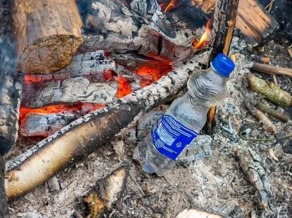 Wasserflasche steht neben glühenden Holzresten eines kleinen Feuers