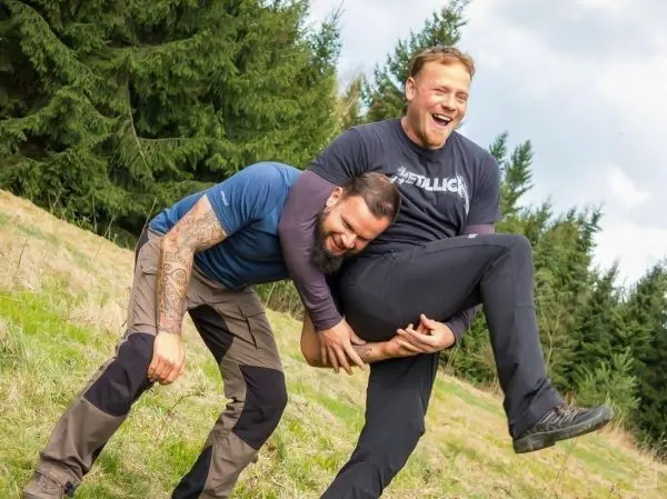 Zwei Männer heben einen anderen Mann an, während sie auf einer Wiese stehen