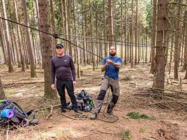 Zwei Personen arbeiten an einer selbstgebauten Seilquerung zwischen Bäumen