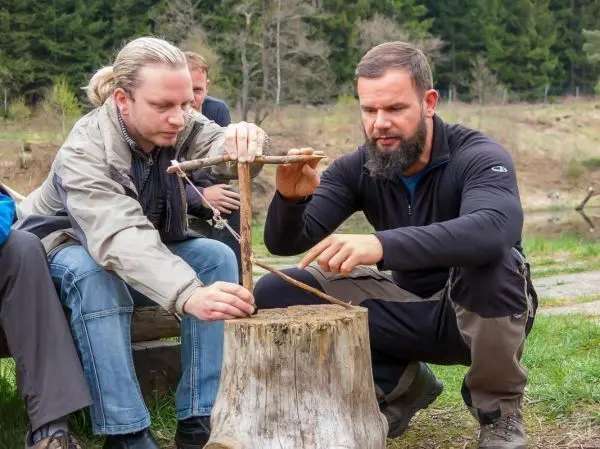 Zwei Personen bauen eine Feuerstelle aus Holzstücken zusammen beim Survival Training