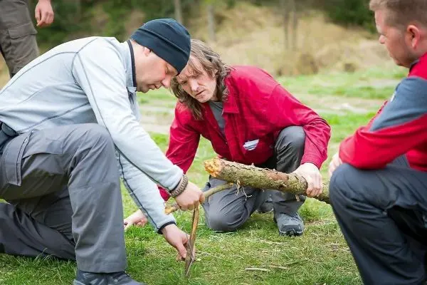 Zwei Personen bearbeiten einen Stock mit einem Messer auf dem Boden