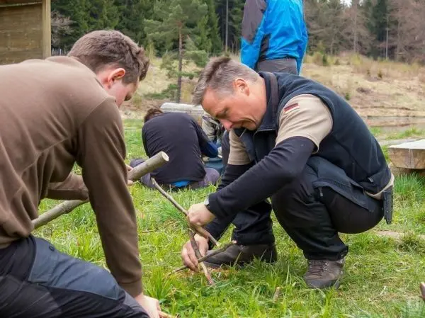 Zwei Personen bearbeiten Holzstücke auf einer Wiese mit Werkzeug
