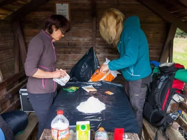 Zwei Personen bereiten Lebensmittel auf einem Tisch in einer Unterstandshütte vor