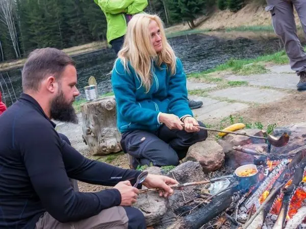 Zwei Personen sitzen am Lagerfeuer und bereiten Essen in einem Topf zu