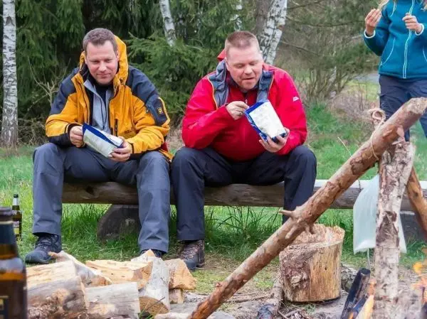 Zwei Personen sitzen auf einer Holzbank und essen aus Tüten, Feuer brennt