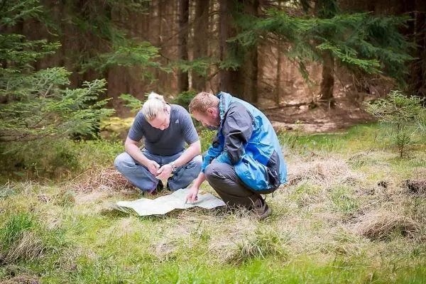 Zwei Personen studieren eine Karte auf dem Boden im Wald