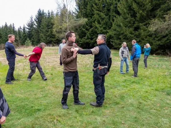 Zwei Personen üben eine körperliche Technik im Freien, während andere Teilnehmer in der Umgebung stehen