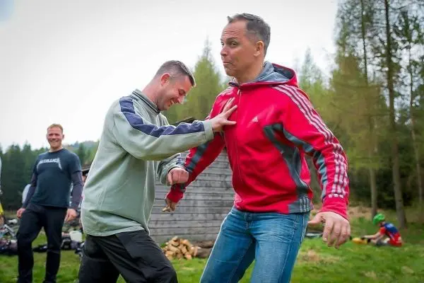 Zwei Personen üben eine körperliche Technik in einer Waldumgebung