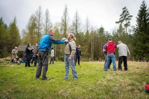 Zwei Personen üben eine Technik im Freien, umgeben von weiteren Teilnehmern