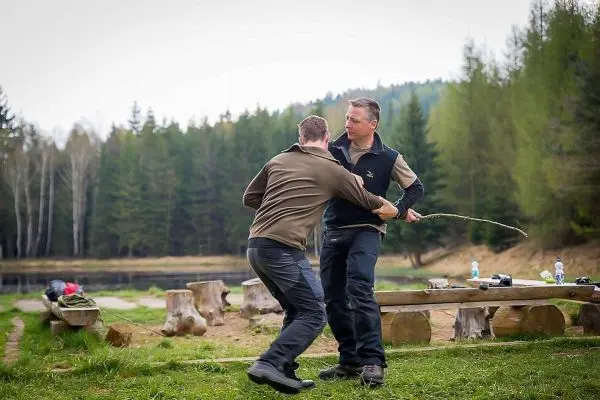 Zwei Personen üben eine Technik mit einem Stock in einer Waldumgebung