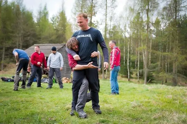 Zwei Personen üben eine Technik zur Kontrolle in einer Wiese, weitere Teilnehmer im Hintergrund