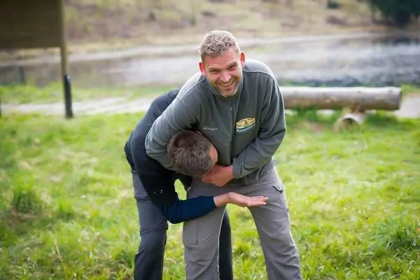 Zwei Personen üben eine Umklammerungstechnik im Freien auf einer Wiese