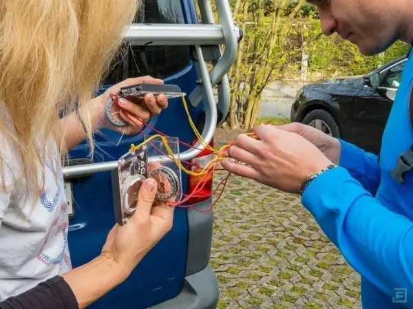 Zwei Personen verbinden elektrische Kabel an einem Gerät in der Nähe eines Fahrzeugs
