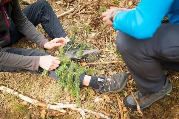 Zweige werden um einen Fuß gewickelt, während eine Person assistiert