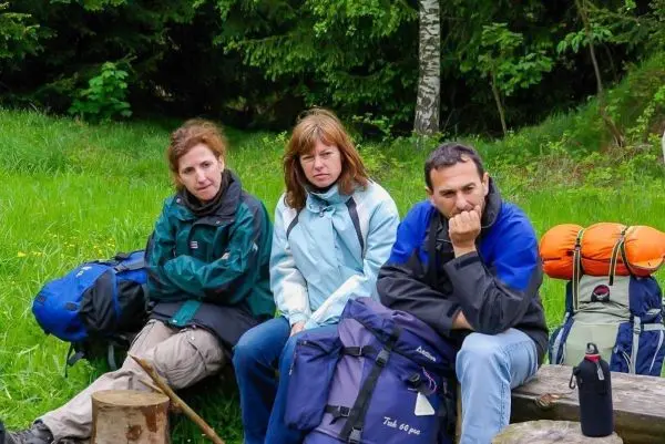 Drei Personen sitzen auf Baumstümpfen mit Rucksäcken im Grünen