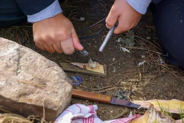 Feuerstahl erzeugt Funken auf Zunder in der Erde, während ein Messer daneben liegt