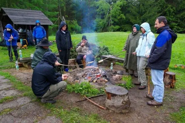 Gruppe von Personen sitzt um ein Feuer und grillt mit Stöcken beim Überlebenstraining