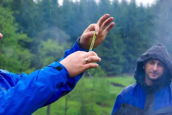 Hände halten eine Schnur, während im Hintergrund Bäume und Regen sichtbar sind