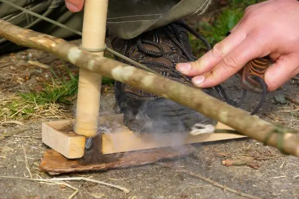 Holzfeuerbohrer erzeugt Rauch auf Zunderplatte durch Reibung