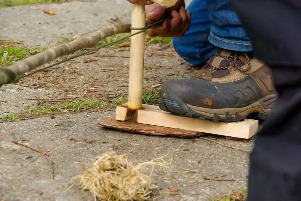 Holzstück mit Bohrer und Zunder für Feuerbohrer-Technik vorbereitet