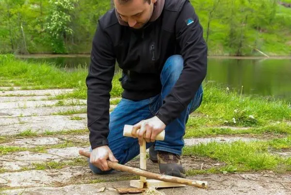 Holzstück wird mit einem anderen Stock bearbeitet, um Zunder zu erzeugen