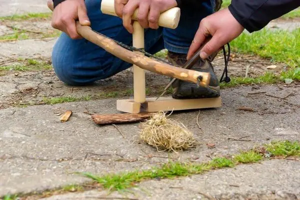 Holzstück wird mit einem Feuerbohrer bearbeitet, Zunder liegt bereit