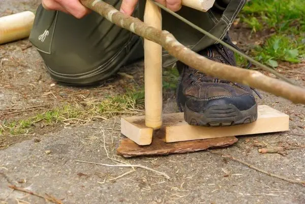 Holzstück wird mit einem Stock bearbeitet, um Glut zu erzeugen