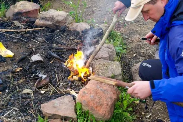 Kleine Flamme entzündet Zunder mit Holzstück in Feuerstelle